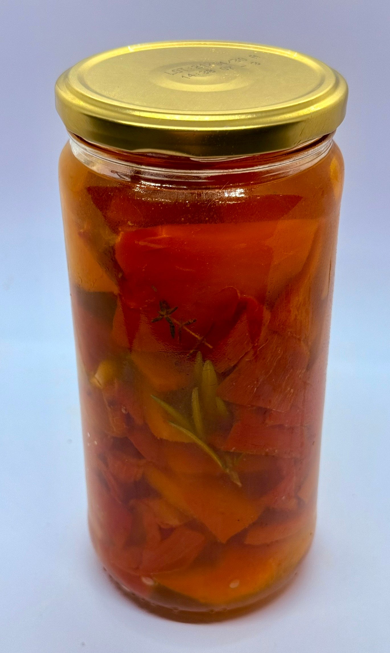 Glanzende rode paprikarepen in een glazen pot, overgoten met olijfolie, knoflook en verse kruiden.