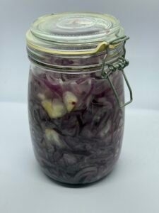 Een glazen pot met felroze uienringen als resultaat van gefermenteerde rode ui maken.