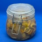 Een weckpot gevuld met het resultaat van ingelegde mosselen maken, omringd door uienringen en zwarte peperkorrels.