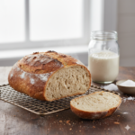 Een aangesneden glutenvrij rijstmeel brood op een rooster, met een luchtige kruim en een pot rijst-zuurdesemstarter op de achtergrond.